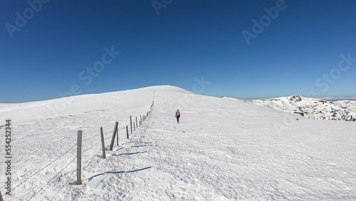 Woman hiking along fence on snow covered alpine meadow near Ladinger Spitz, Saualpe, Lavanttal Alps, Carinthia, Austria, Europe. Trekking in Austrian Alps in winter. Ski touring and snow shoe tourism © Chris
