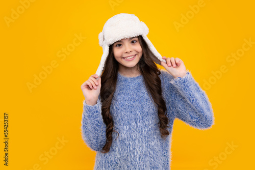 Teenager girl with winter hat over isolated yellow background. Winter christmas holidays, new year mood. Kids warm clothes. Happy teenager, positive and smiling emotions of teen girl.