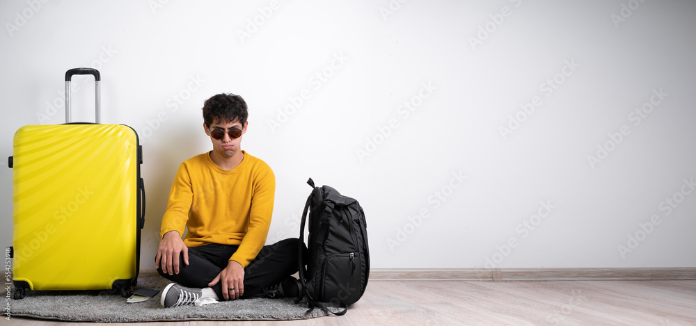 Dissatisfied passenger with a yellow suitcase sits upset about a failed trip on a white background. Air travel concept Dissatisfied passenger with a yellow suitcase sits upset about a failed trip on a white background. Air travel concept