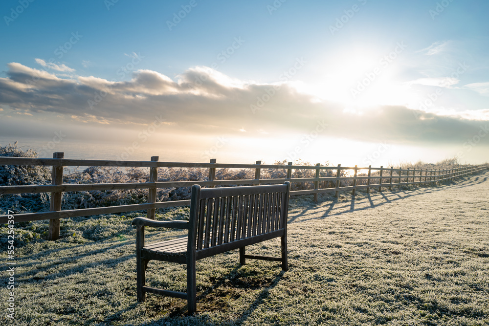 Isolated wooden park bench seen on a cliff overlooking a cold North Sea during early morning.