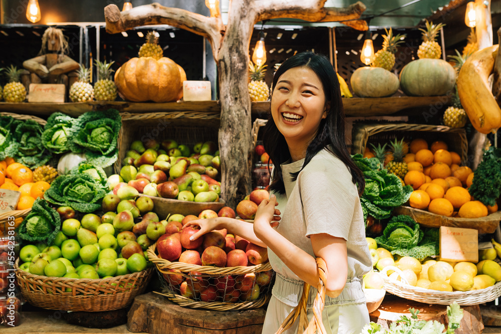 Obraz premium Laughing Asian woman on an outdoor market. Smiling female buying organic food.