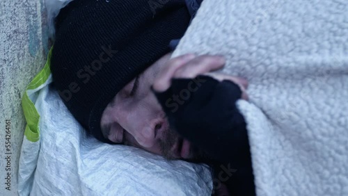Homeless man sleeps on the street. Poorly and dirtily dressed, he freezes as he lies on the cold ground.