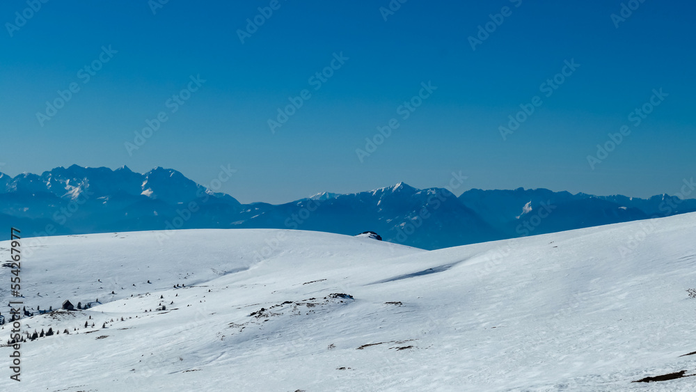 Panoramic view on summit cross of mountain peak Grosser Sauofen in winter on Saualpe, Lavanttal Alps, Carinthia, Austria, Europe. Snowcapped mountain ranges of Karawanks and Kamnik Savinja Alps