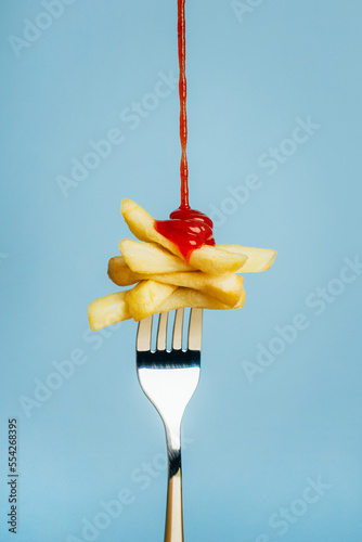 close-up on french fries with pouring ketchup on a fork on a blue background