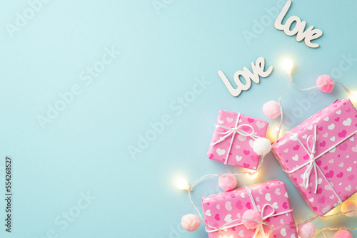 St Valentine's Day concept. Top view photo of gift boxes light bulb garland inscriptions love and fluffy pompons on isolated pastel blue background with empty space