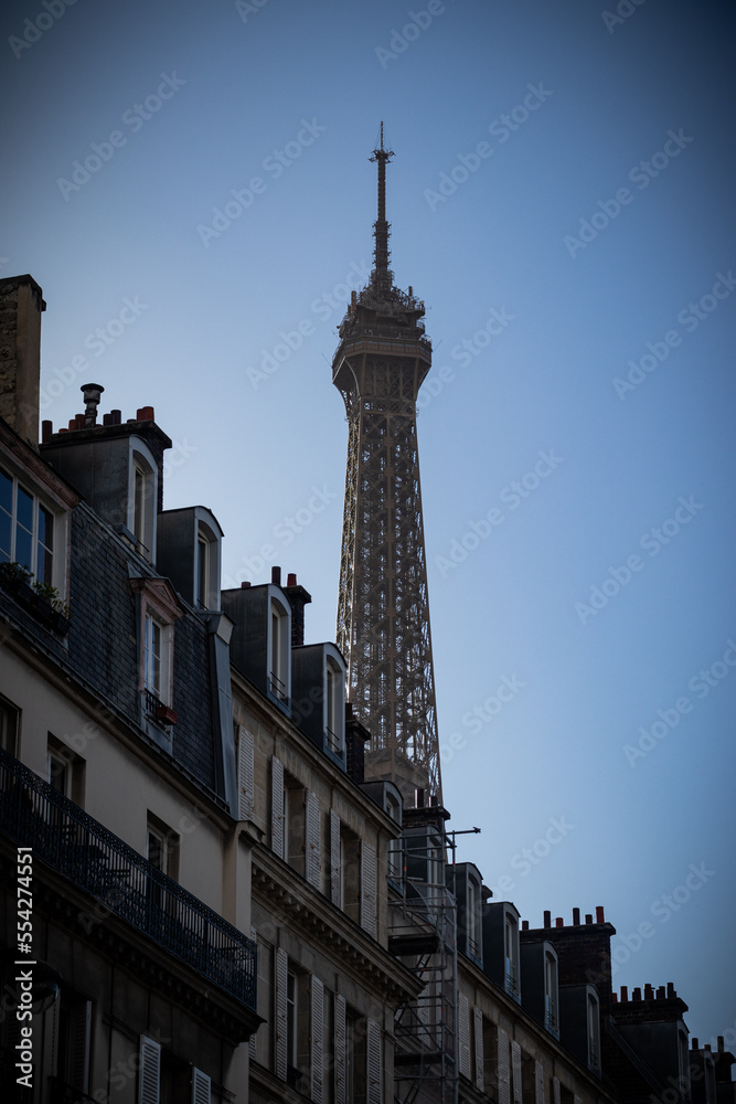 The top of the Eiffel Tower towering above the roofs of Parisian buildings