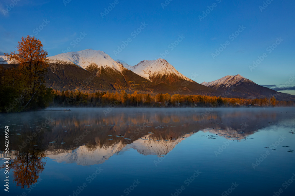 Tranquil Lake Kathlyn surrounded by autumn coloured trees and snow-capped Coast Mountains, viewed from Lakedrop Inn, Watson's Landing, BC, Canada; Smithers, British Columbia, Canada