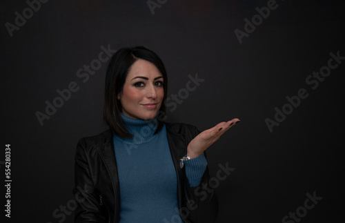 Fotografie bellissima ragazza mora con maglione azzurro e fondo nero e copy space che indic
