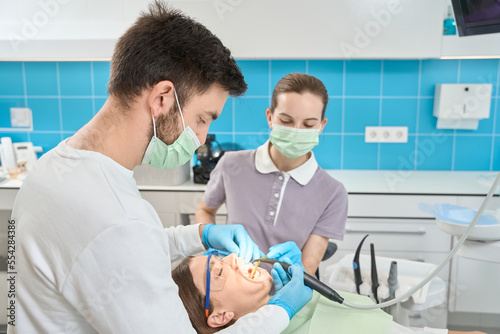 Dental conducting teeth-whitening procedure on client assisted by nurse