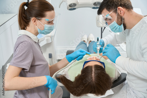 Male dentist is giving anesthesia to woman aided by assistant