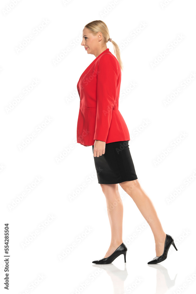 Middle aged senior business woman in red jacket and black skirt walking on white background. Side, profile view. Middle aged senior business woman in red jacket and black skirt walking on white background. Side, profile view.