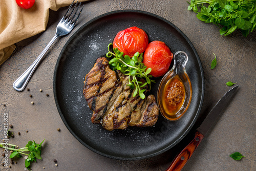 Fried pork loin with sauce and grilled tomatoes on black plate top view