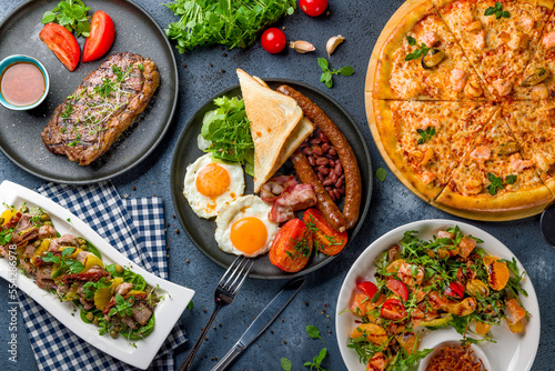 English Breakfast on a plate, pizza with seafood, salad with orange and salmon, steak striploin, salad with duck top view © Алиса Королевская