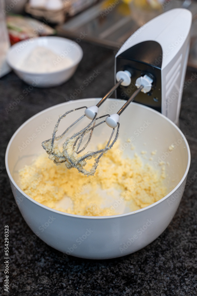 Mix the butter with the sugar in a white bowl to bake the cake. Blender beater closeup. Selected focus. Mix the butter with the sugar in a white bowl to bake the cake. Blender beater closeup. Selected focus.