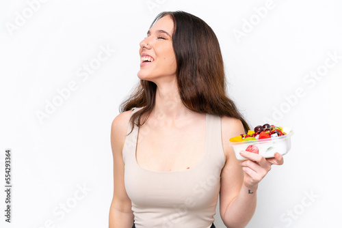 Young caucasian woman holding a bowl of fruit isolated on white background laughing in lateral position