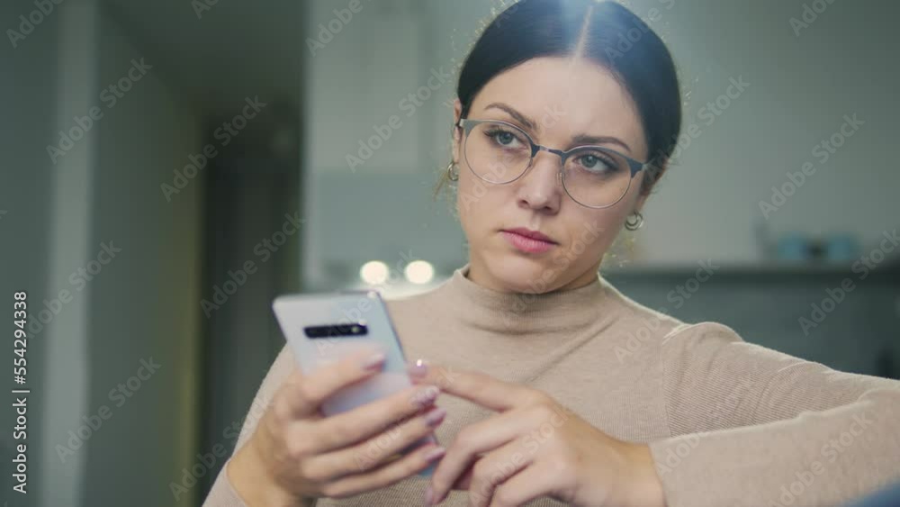 Upset woman marketing manager in big eyeglasses having problems with online orders in social network shop, thinking about problem solution working on smartphone from home Upset woman marketing manager in big eyeglasses having problems with online orders in social network shop, thinking about problem solution working on smartphone from home
