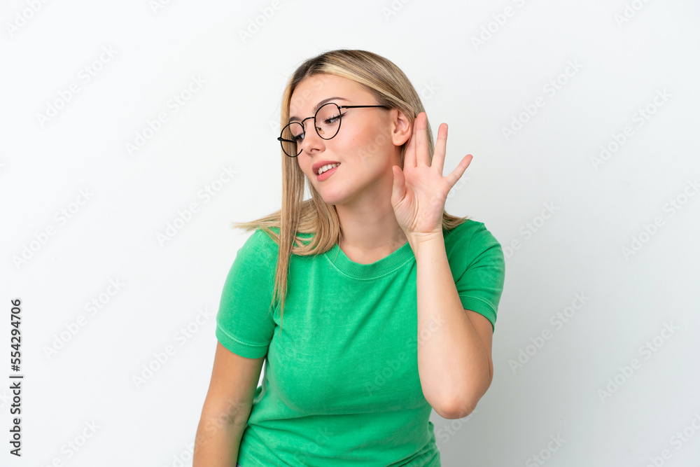 Young caucasian woman isolated on white background listening to something by putting hand on the ear