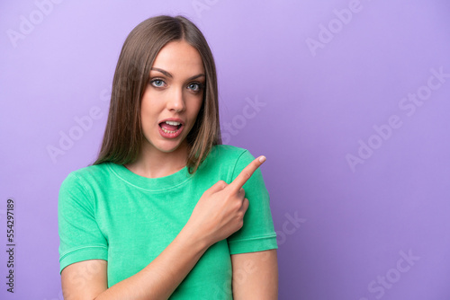 Young caucasian woman isolated on purple background surprised and pointing side