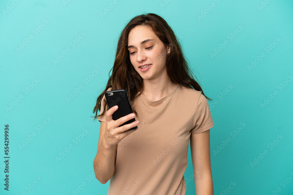 Young caucasian woman isolated on blue background sending a message or email with the mobile Young caucasian woman isolated on blue background sending a message or email with the mobile