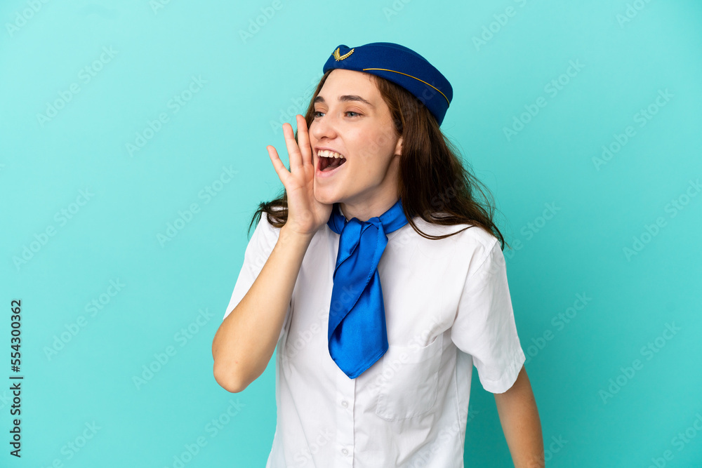Airplane stewardess woman isolated on blue background shouting with mouth wide open to the lateral Airplane stewardess woman isolated on blue background shouting with mouth wide open to the lateral