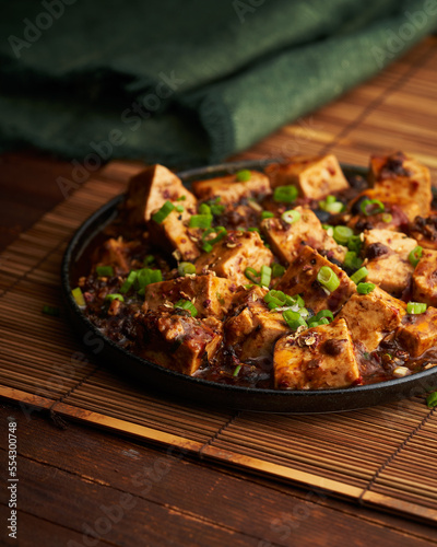A sizzling plate of mapo tofu, garnished with spring onions on a wooden mat, exuding authentic Sichuan flavors, perfect for culinary stock photography.