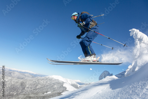 Skier skiing and jumping downhill in high mountains against blue sky