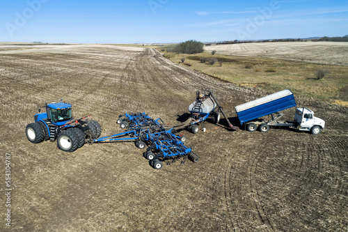 Aerial view of farmer filling an air seeder hopper with a truck in a field with blue sky in the background; Beiseker, Alberta, Canada photo