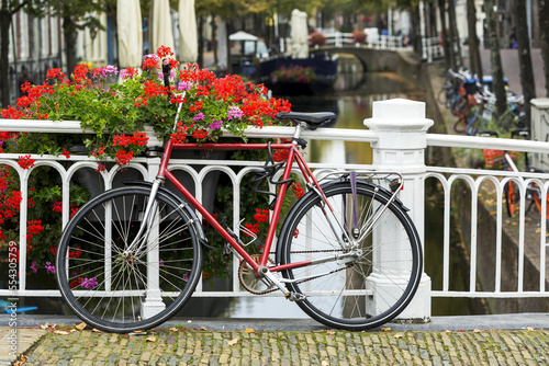 Bike along white metal railing on stone bridge with colourful flowers in box and canal in the background below; Delft, South Holland, Netherlands photo