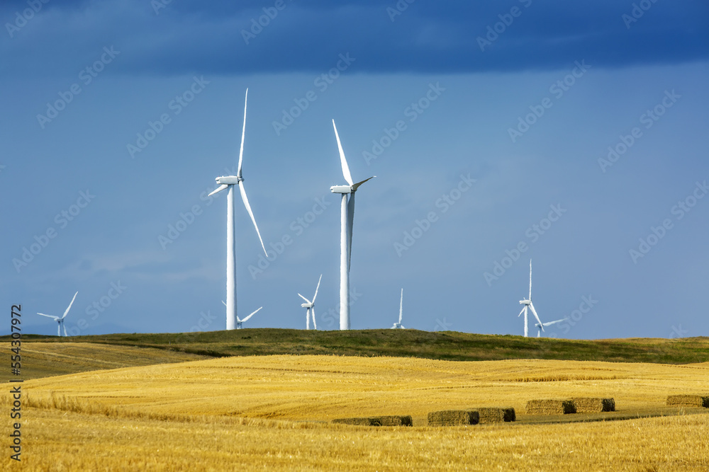 Large metal wind turbines on rolling hills with blue sky, North of Waterton; Alberta, Canada Large metal wind turbines on rolling hills with blue sky, North of Waterton; Alberta, Canada