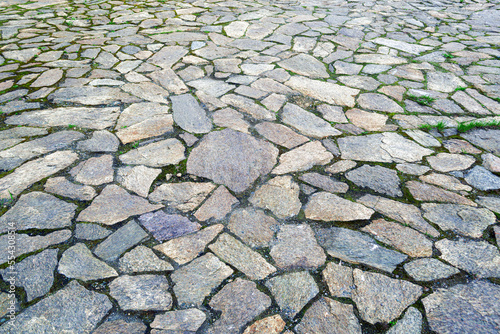 The texture of the stone pavement with grass between the stones close-up.