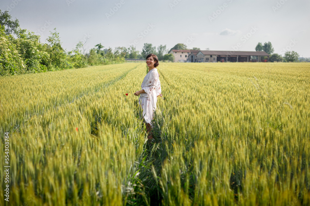 lauphing woman with short hair in white dress walking in wheat field