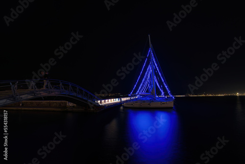 Fototapeta Naklejka Na Ścianę i Meble -  Christmas atmosphere and cityscape of the city of Volos with blue lights illuminating the boats and sailboats, decorating the beautiful beach town. Volos Magnesia, Greece