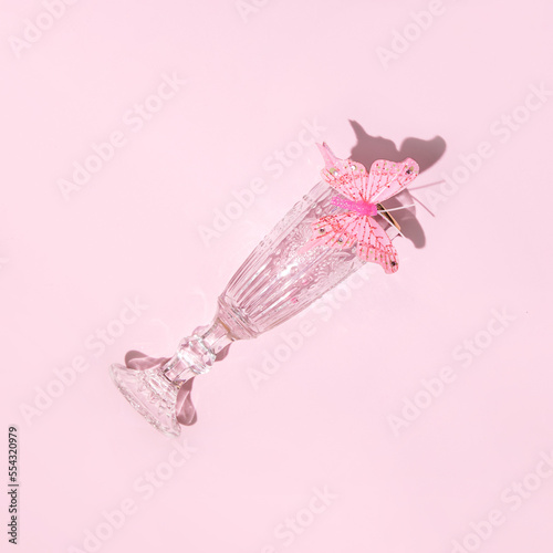 Retro aesthetic style layout; champagne glass decorated with  butterfly; romantic spring or summer party concept. Pastel pink background. 