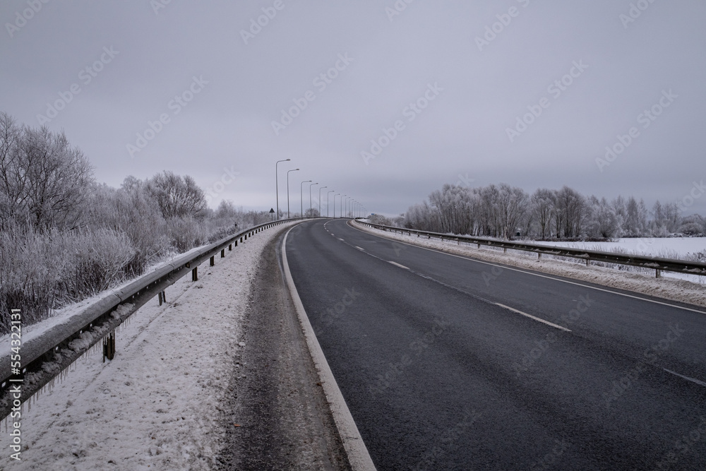 clean wet asphalt road in wintertime. Dirty snow on road sides. Long far perspective. Latvia landscape near Jelgava town. Bypass road 