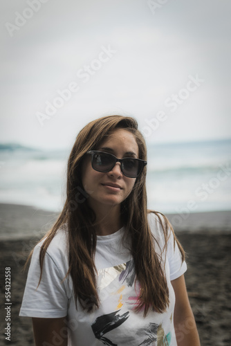 Portrait of a woman with sunglasses, on the beach, wearing a white shirt.