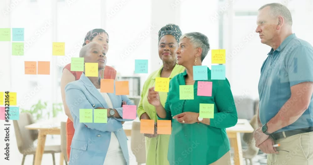 Sticky notes, teamwork and business people working on strategy in office. Collaboration, planning or group of employees with mature female leader writing sales ideas on glass wall in modern workplace Sticky notes, teamwork and business people working on strategy in office. Collaboration, planning or group of employees with mature female leader writing sales ideas on glass wall in modern workplace