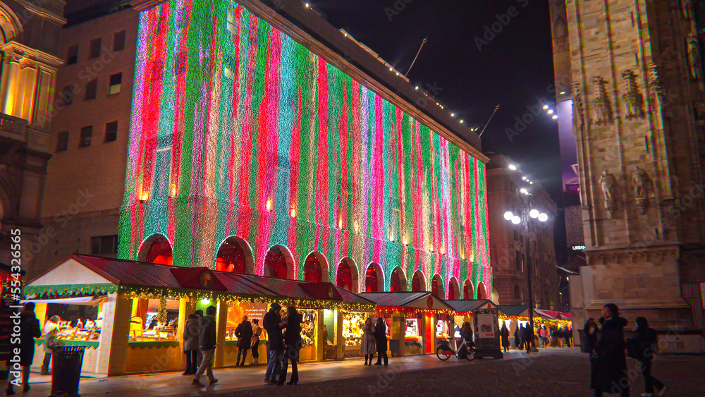 Obraz premium People buy gifts at the festive Christmas market in the city center Albero di Natale Christmas tree with colorful lights. City at night. One night ahead. Multicolored lights. Milan Italy December 2022