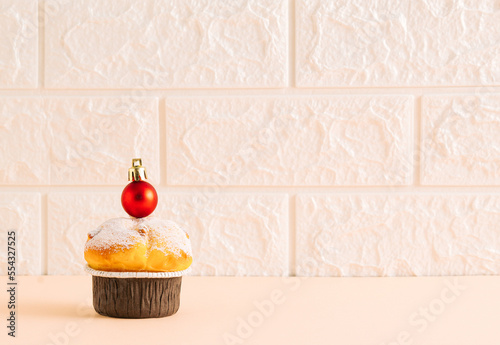 Minimal holiday concept made of cupcake with red Christmas bauble on table. New year food concept. Brick wall background. Copy space.