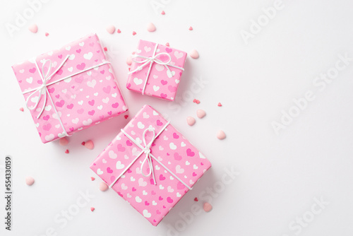 Saint Valentine's Day concept. Top view photo of pink gift boxes in wrapping paper with heart pattern and sprinkles on isolated white background © ActionGP
