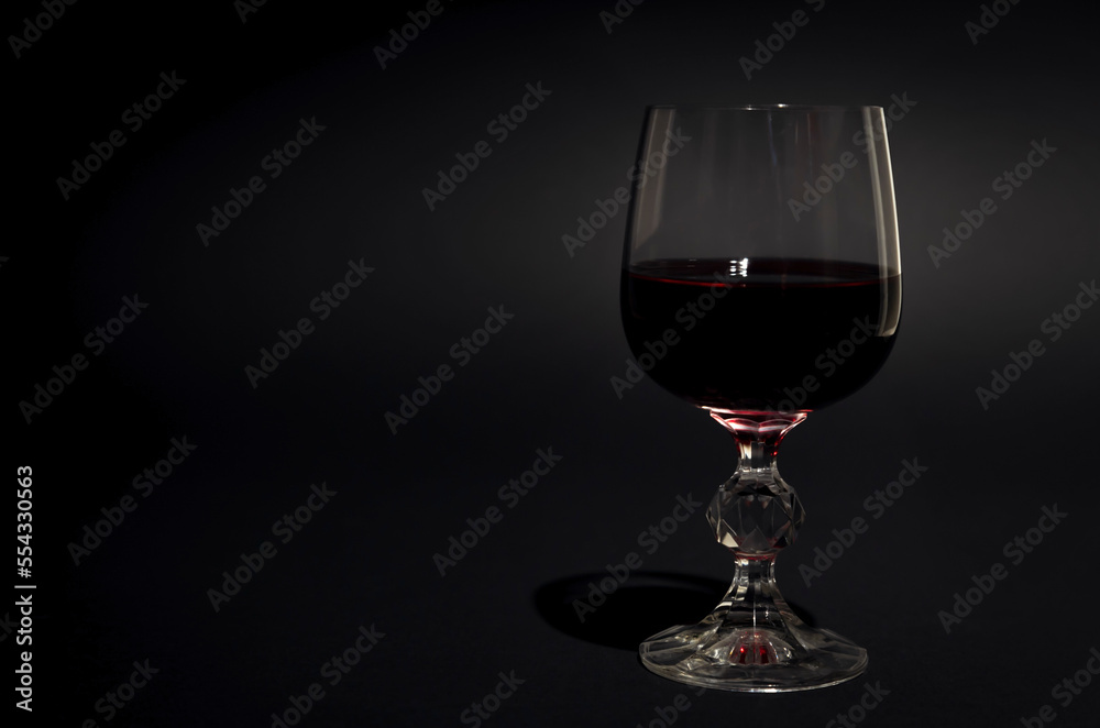 A glass of red wine. Red wine in a transparent glass with reflections. Black background. Focus on the glass. A glass of red wine. Red wine in a transparent glass with reflections. Black background. Focus on the glass.