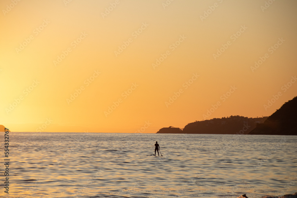 Man practicing Stand Up Paddle with a beautiful orange sunset