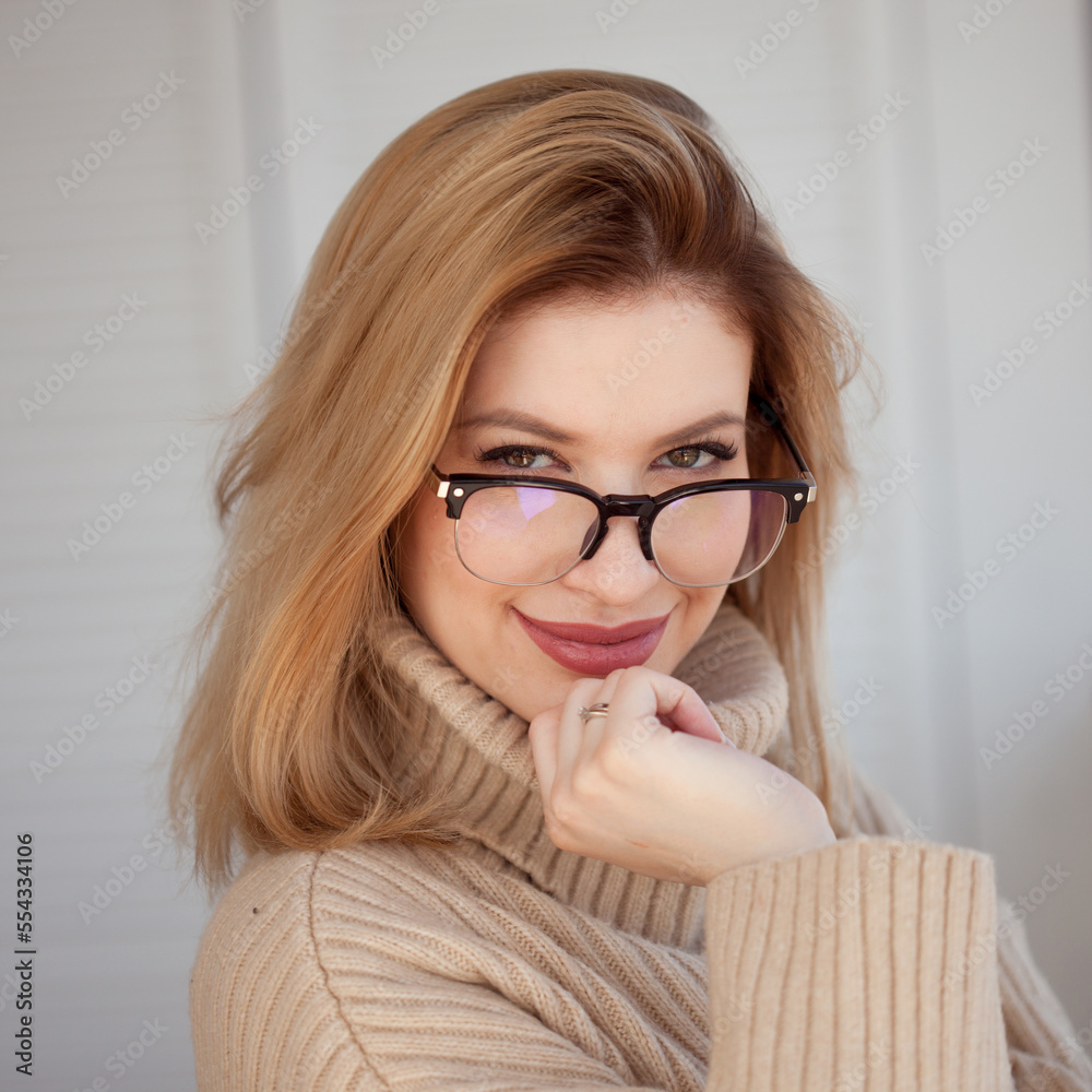 Young cute blonde with eyeglasses and a beige sweater. Stylish fashionable young woman. woman with glasses smiling Young cute blonde with eyeglasses and a beige sweater. Stylish fashionable young woman. woman with glasses smiling