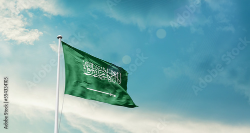 Waving Flag of Saudi Arabia in Blue Sky. The symbol of the state on wavy cotton fabric.