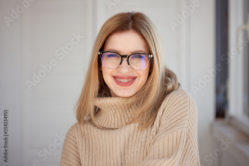 Young cute blonde with eyeglasses and a beige sweater. Stylish fashionable young woman. woman with glasses smiling