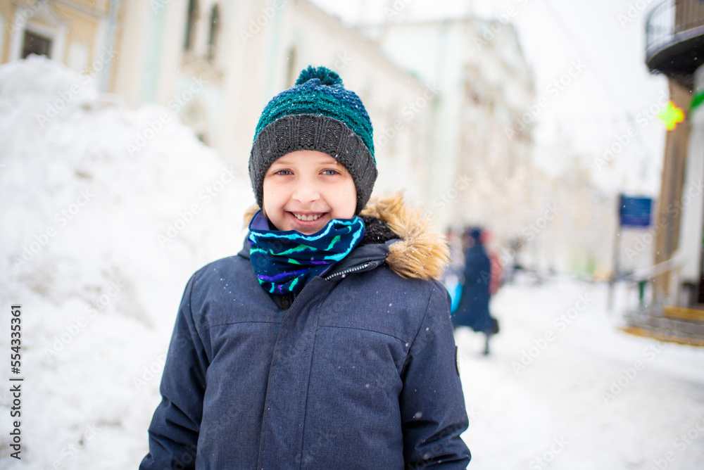 smiling happy boy in winter clothes walking in snow city