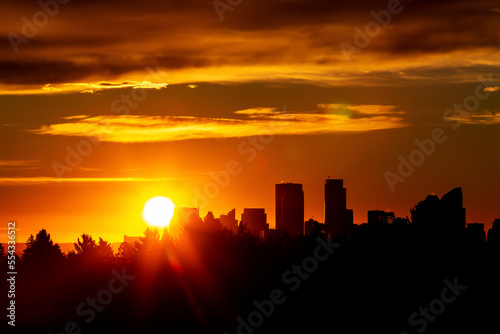 Dramatic colourful sky with a silhouetted cityscape and sunburst; Calgary, Alberta, Canada