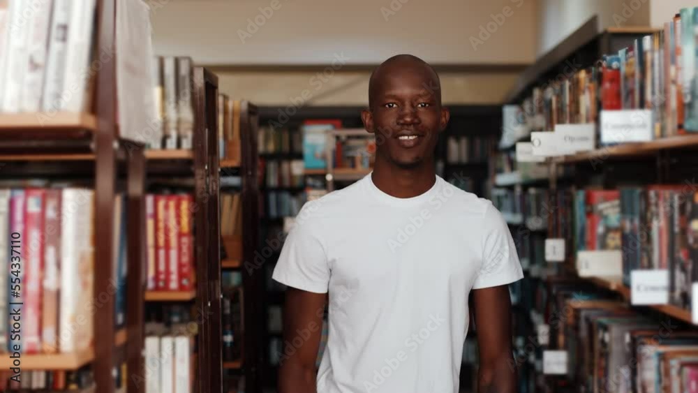 Black man in library turns and looks at camera smiles, standing between the shelves and cabinets with books. Concept of education Black man in library turns and looks at camera smiles, standing between the shelves and cabinets with books. Concept of education