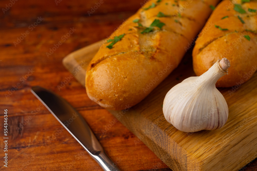 Close-up of fresh cheese garlic bread with garlic butter and aromatic herbs on a wooden board on a wooden table. Close-up of fresh cheese garlic bread with garlic butter and aromatic herbs on a wooden board on a wooden table.