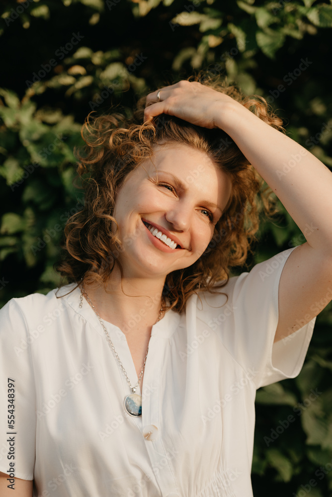 A woman with curly hair is posing in the park at the sunset.