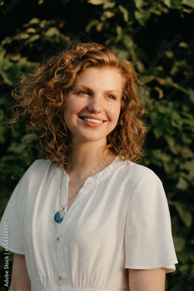 A woman with curly hair is posing in the park at the sunset.